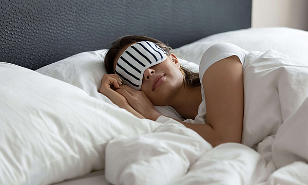 Stilvolle Nachthemden. Komfortable Schlafmaske, die jungen Touristenreisenden eine gesunde Nachtruhe ermöglicht, die sie an einem neuen Platz im Hotelsuite-Zimmer verbringen können, tausendjährige Frau, die in einem großen Kingsize-Bett mit Augenmaske schläft.