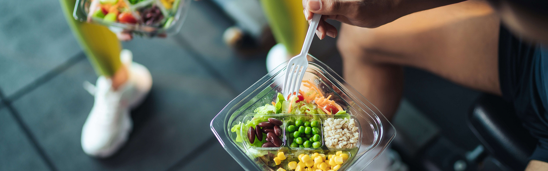 Top-Blick asiatische Mann und Frau gesund essen Salat nach der Übung im Fitnessraum. Zwei Sportler essen zusammen Salat für Gesundheit. Selektiver Fokus auf Salatschüssel zur Verfügung.
