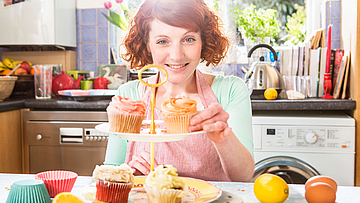 Frau sitzt für einem Tablett mit Muffins und lächelt vor Glück