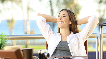Frau sitzt mit einem zufriedenem Gesichtsausdruck auf dem Balkon.