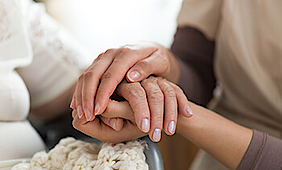 Nahaufnahme einer Frau, die die Hand einer älteren Dame umfasst.