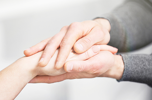 Die Hände einer jungen Person umfassen eine Hand einer älteren Person.