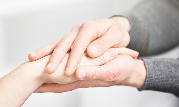Die Hände einer jungen Person umfassen eine Hand einer älteren Person.