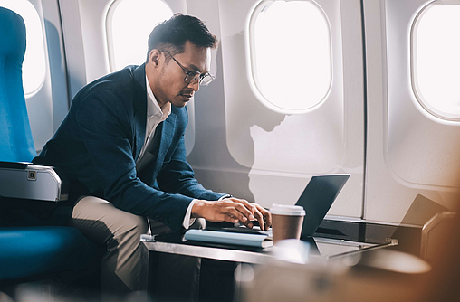 Junger gutaussehender Geschäftsmann mit Notizbuch sitzt in einem Flugzeug.