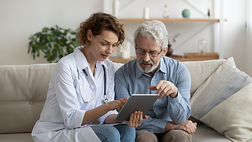 Ärztin und Patient sitzen mit dem Tablett auf dem Sofa und besprechen das Ergebnis der Untersuchung.