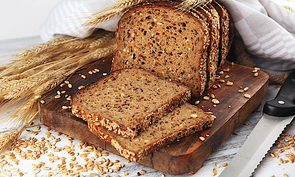 Auf einem Tisch liegt ein Vollkornbrot. Daneben liegt ein Messer. 