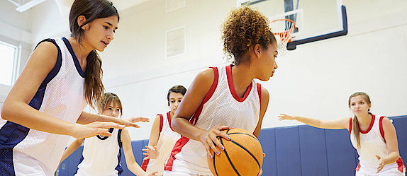 Eine Frauenmannschaft spielt Basketball. Sie sind im Angriff. Der Ball wird gleich in Richtung Korb geworfen. 