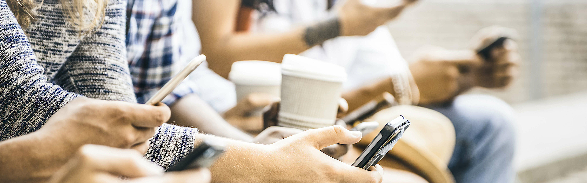 Eine Gruppe junger Menschen sitzt auf einer Mauer. Sie alle haben Smartphones in der Hand und schauen darauf. 