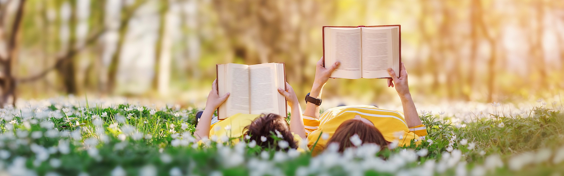 Frau und Kind lesen gemeinsam auf der Wiese Bücher.