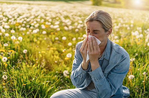 Frau sitzt auf einer Blumenwiese und leiden unter den Symptomen für eine Pollenallergie