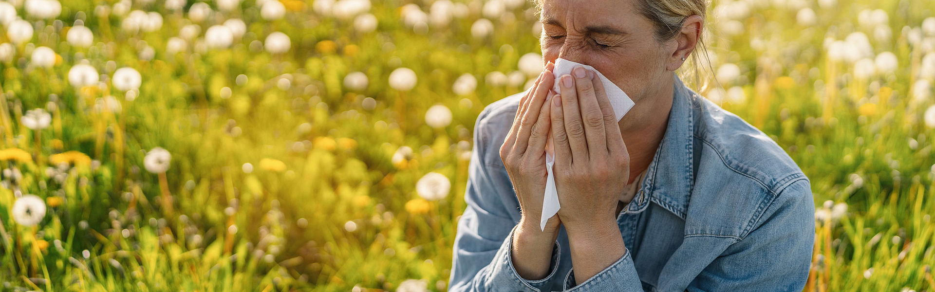 Frau sitzt auf einer Blumenwiese und leiden unter den Symptomen für eine Pollenallergie