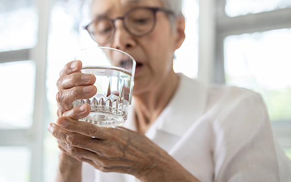 Ältere Frau versucht aus einem Wasserglas zu trinken.