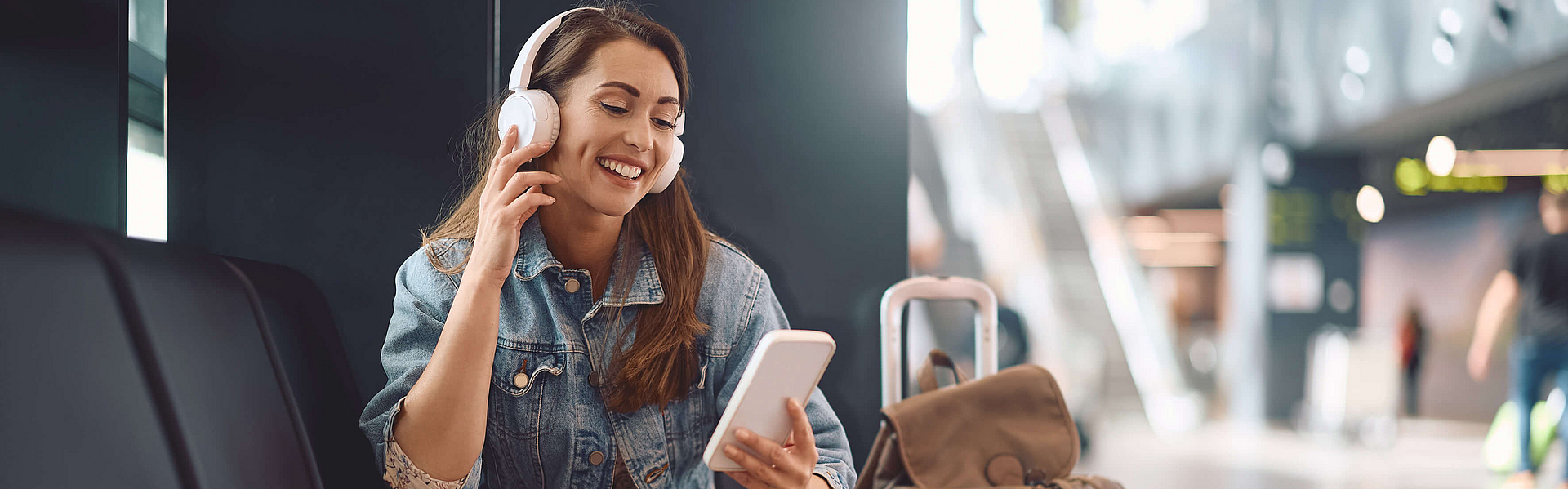 Frau sitzt im Abflugbereich auf dem Weg in den Urlaub. Sie hört Musik über das Smartphone. 