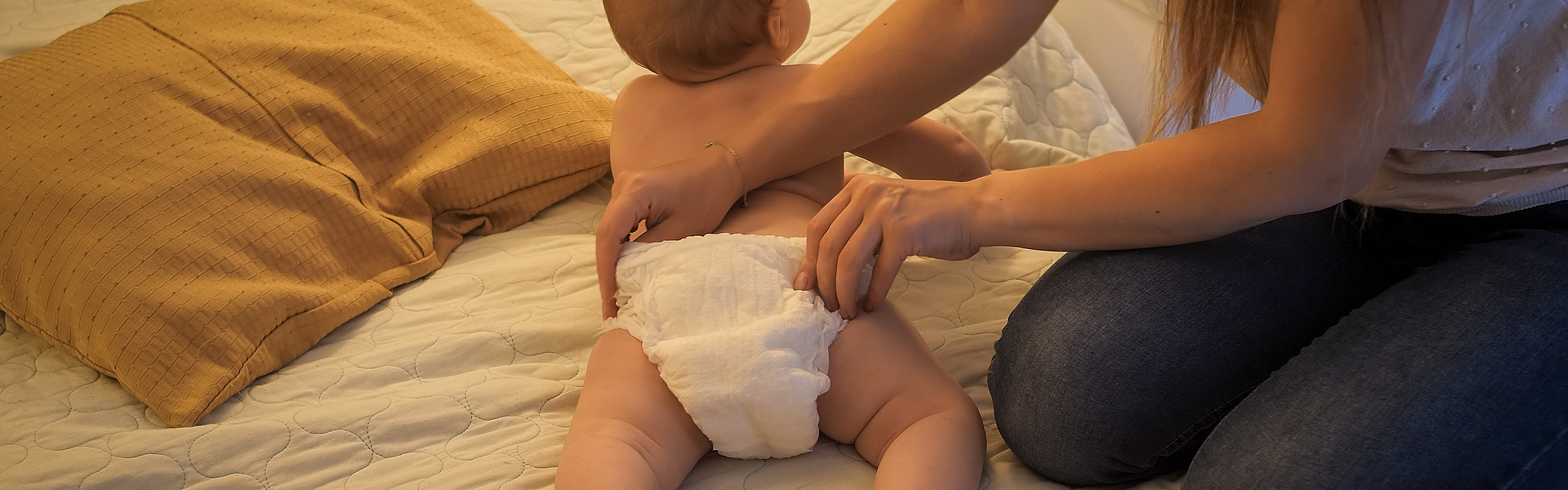 Eine Mutter wechselt die Windeln ihres Kindes auf einem Bett. 