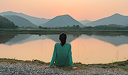 Eine Frau sitzt bei Sonnenuntergang am See