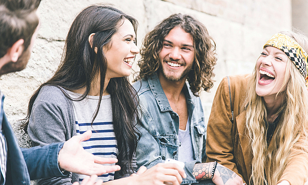 Gruppe von vier Freunden, die laut draußen lachen, es herrscht eine gute und positive Stimmung.
