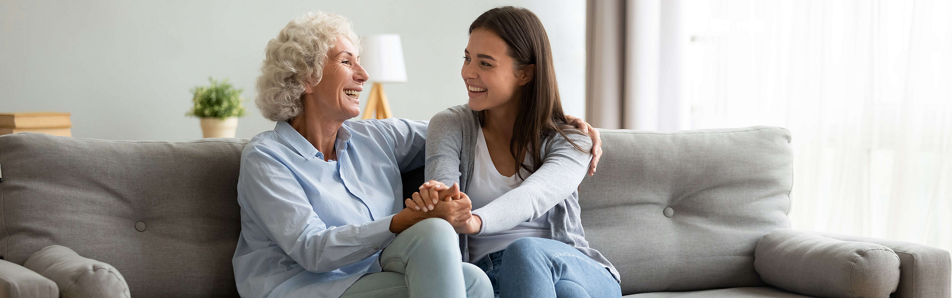 Zwei Frauen, die Spaß beim Unterhalten haben, sitzen auf dem Sofa im modernen Wohnzimmer. 