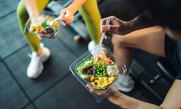 Top-Blick asiatische Mann und Frau gesund essen Salat nach der Übung im Fitnessraum. Zwei Sportler essen zusammen Salat für Gesundheit. Selektiver Fokus auf Salatschüssel zur Verfügung.