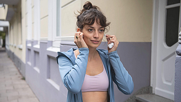 Junge Frau steckt sich kabellose Ohrhörer in die Ohren.