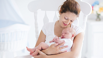 Junge Mutter sitzt mit ihrem Baby auf einem Schaukelstuhl.