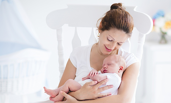 Junge Mutter sitzt mit ihrem Baby auf einem Schaukelstuhl.