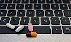 Vier Pillen liegen auf einer Laptoptastatur. Zwei der Pillen sind farbig.