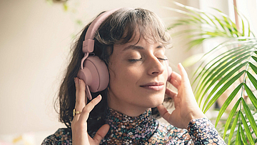 Frau hört über Kopfhörer Musik, sie hat die Augen geschlossen und ist entspannt.