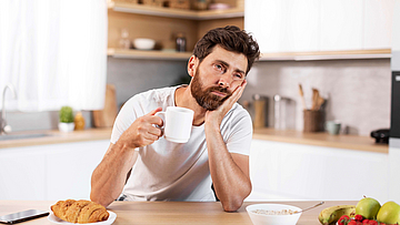 Müder Mann sitzt morgens am Frühstückstisch