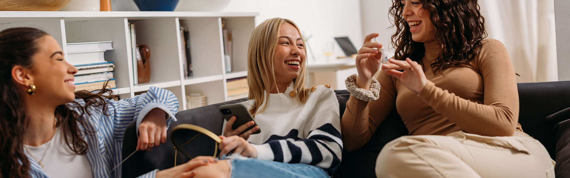 Drei junge, lachende Frauen sitzen auf einem Sofa und unterhalten sich