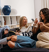 Drei junge, lachende Frauen sitzen auf einem Sofa und unterhalten sich