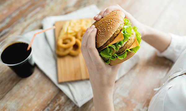 Eine Frau hält einen Hamburger in der Hand. Sie isst Fast Food.