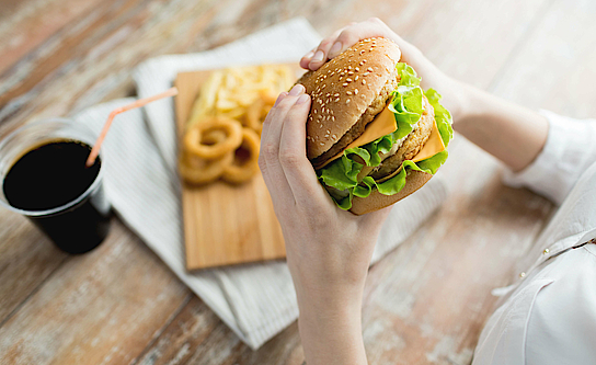 Eine Frau hält einen Hamburger in der Hand. Sie isst Fast Food.