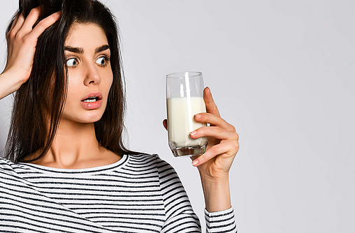 Frau schaut entsetzt auf eine Glas mit Milch, dass sie in der Hand hält. Vermutlich ist sie laktoseintolerant.