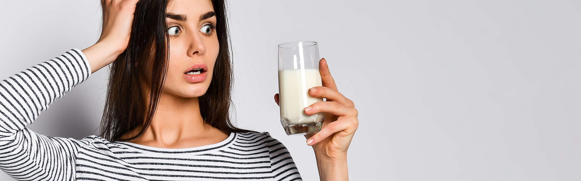 Frau schaut entsetzt auf eine Glas mit Milch, dass sie in der Hand hält. Vermutlich ist sie laktoseintolerant.