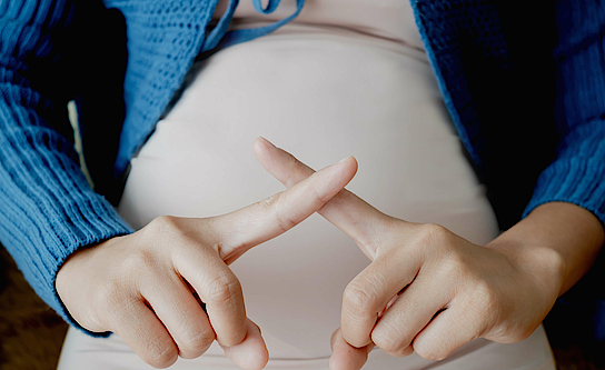 Schwangere Frau symbolisiert ein X-Zeichen.