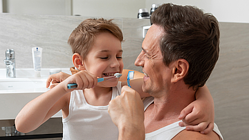 Ein Mann und ein Junge putzen im Badezimmer gemeinsam die Zähne. 