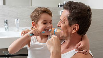Ein Mann und ein Junge putzen im Badezimmer gemeinsam die Zähne. 