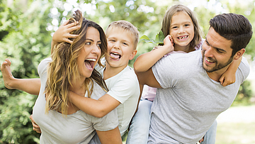 Junge Familie im Park. Die Kinder werden von den Eltern getragen.