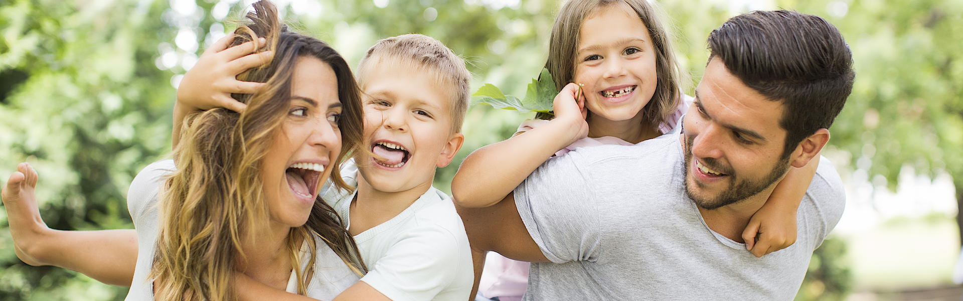 Junge Familie im Park. Die Mutter trägt den Sohn und der Vater trägt die Tochter huckeback.