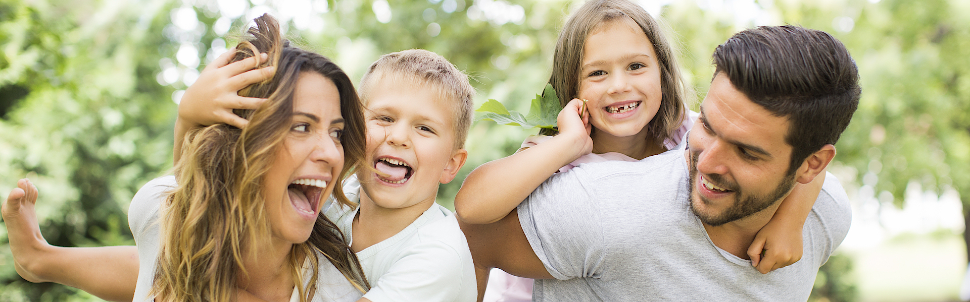 Junge Familie im Park. Die Mutter trägt den Sohn und der Vater trägt die Tochter huckeback.