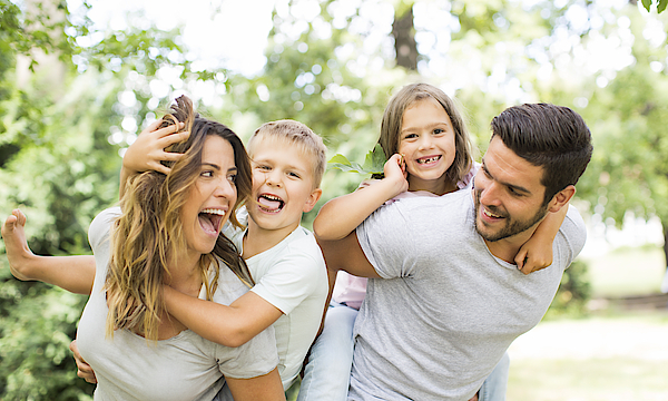 Junge Familie im Park. Die Mutter trägt den Sohn und der Vater trägt die Tochter huckeback.