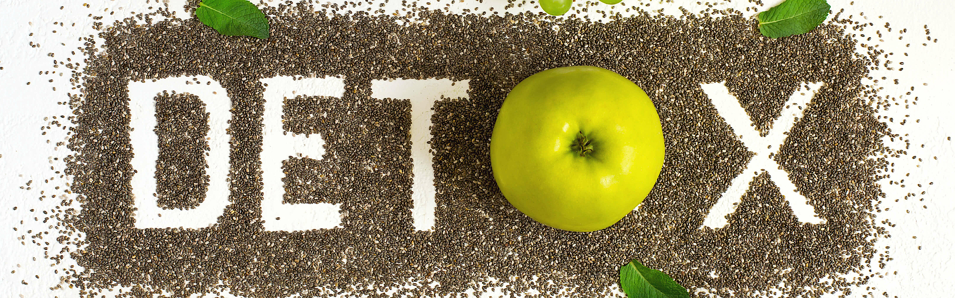 Das Wort Detox ist aus Samen gelegt. Drum herum liegen Äpfel, Trauben und andere Lebensmittel, die angeblich entgiftend wirken.