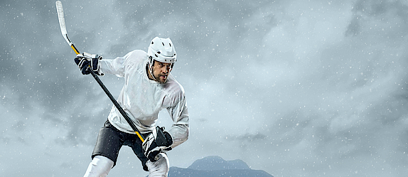 Ein Eishockeyspieler steht auf dem Eis. Er holt mit dem Schläger aus, um den Puk zu spielen.