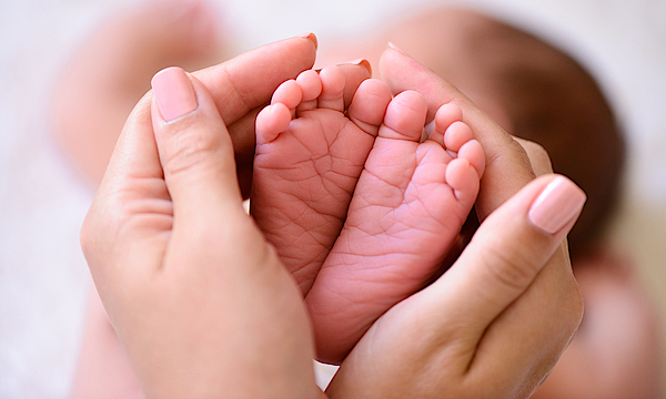 Hände umfassen die kleinen Füße von einem Baby.