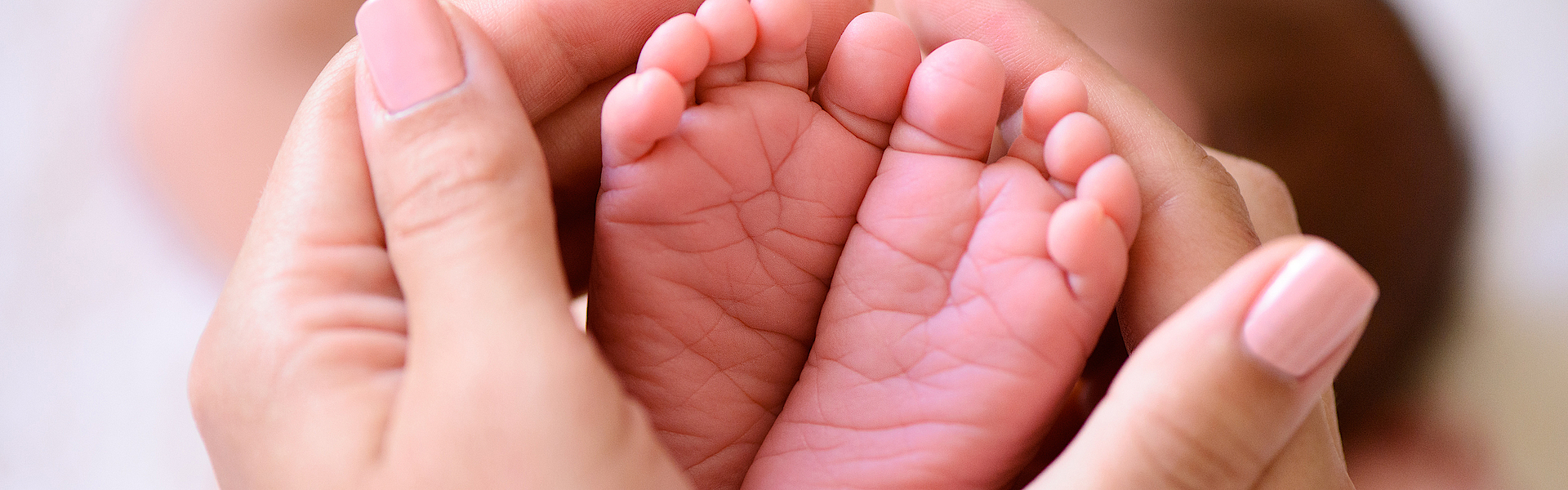Hände umfassen die kleinen Füße von einem Baby.