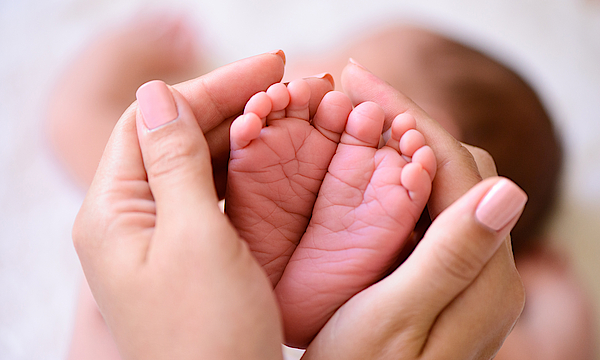 Hände umfassen die kleinen Füße von einem Baby.