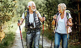Ein glücklich aussehendes älteres Paar wandert in der Natur mit Nordic Walking Stöcken. Mann und Frau tragen einen Rucksack. Sie sehen glücklich aus.