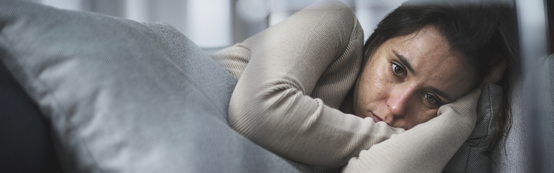 Frau liegt traurig und nachdenklich auf einem Sofa.