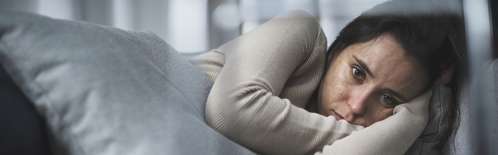 Frau liegt traurig und nachdenklich auf einem Sofa.