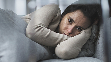 Frau liegt traurig und nachdenklich auf einem Sofa.